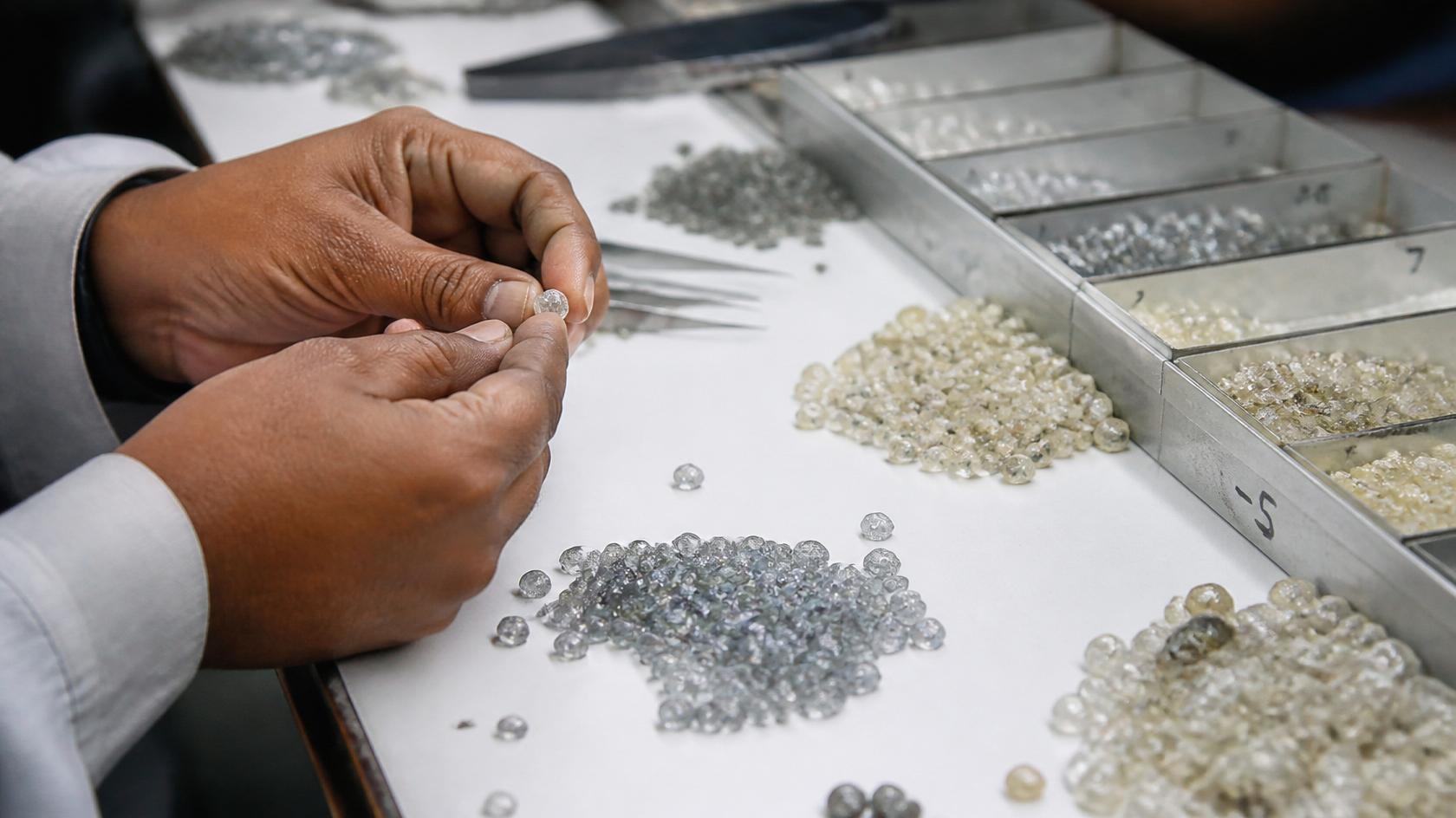 A worker sorting rough gemstones by size and quality into metal trays on a work table