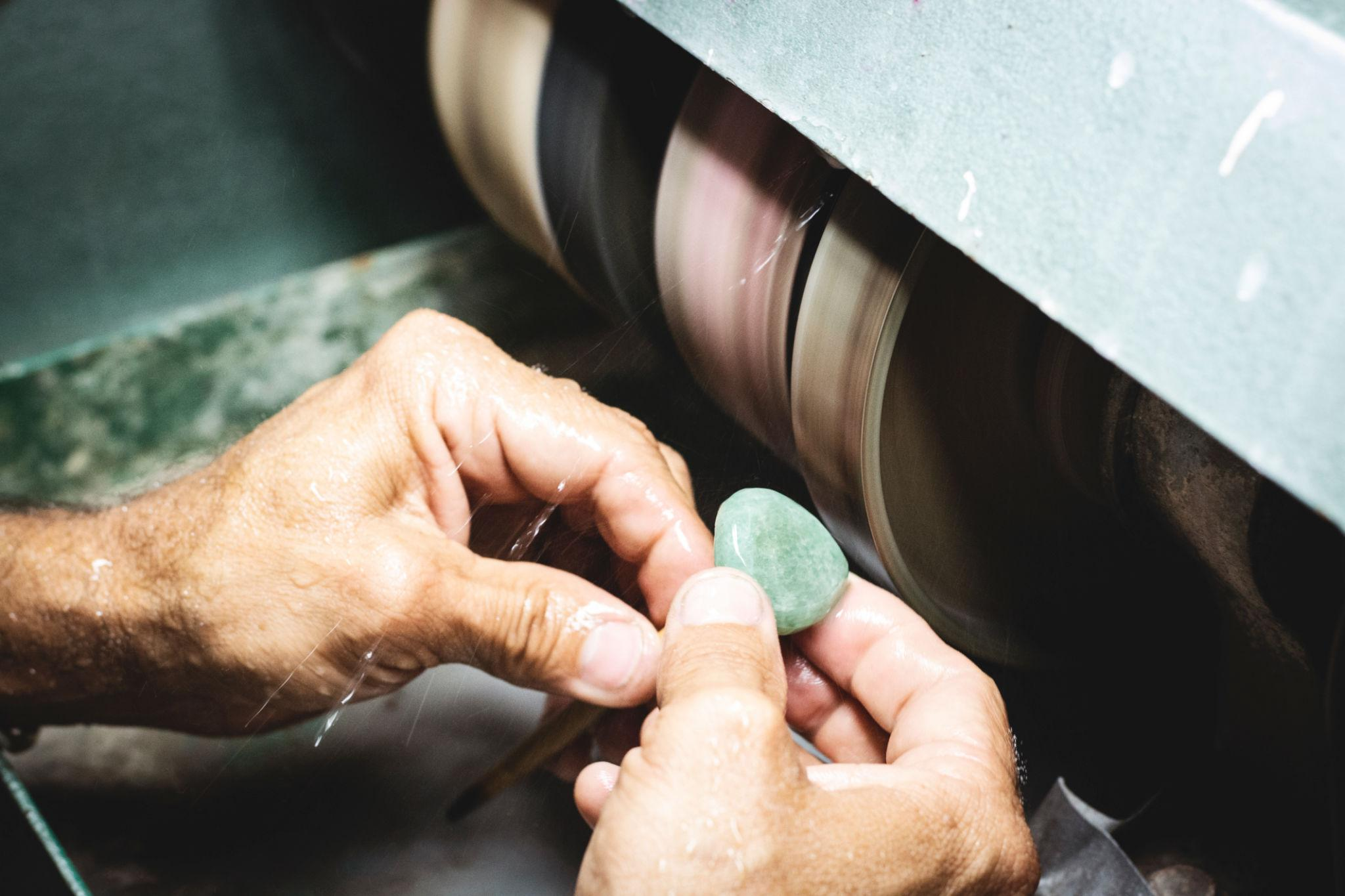 A cutter shaping a stone by hand against a wet polishing wheel